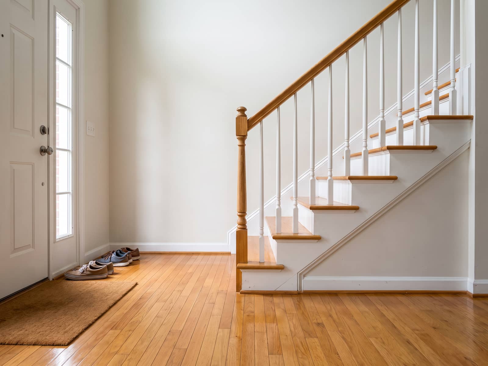 Entryway after a clean, mopped hardwood with an even sheen and dusted stair spindles